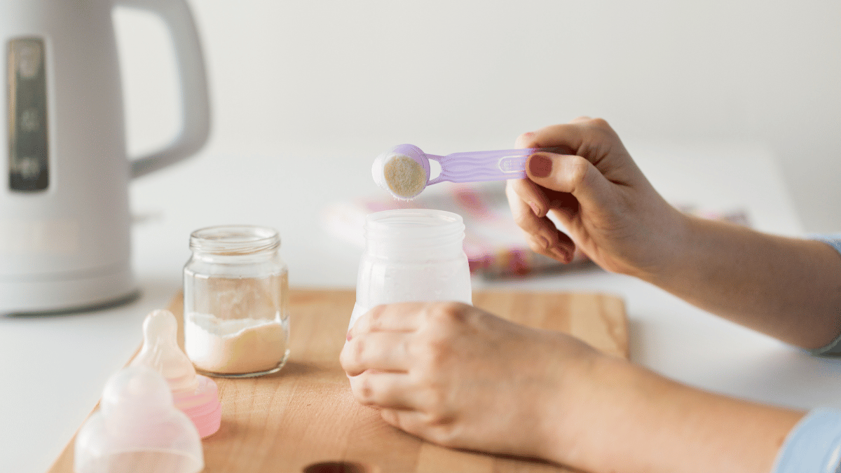 formula milk powder being scooped into baby bottle