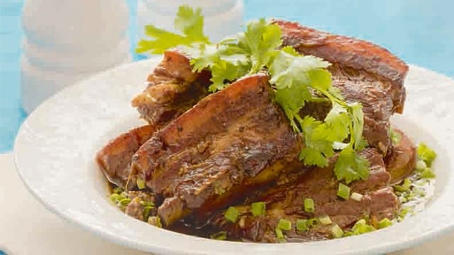 asian style pork belly in a white bowl topped with parsely 